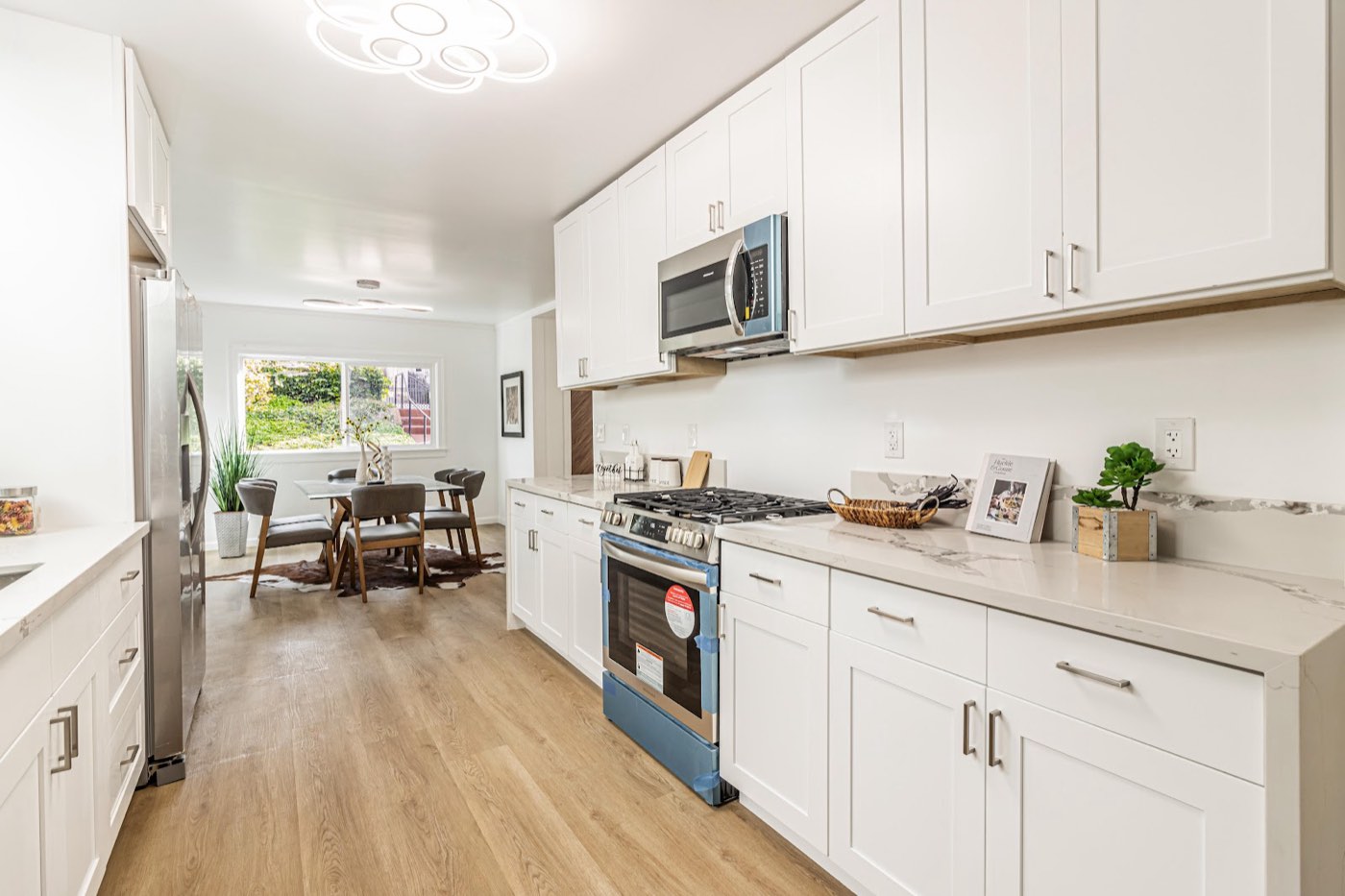 Remodeled white galley kitchen with marble counters and new appliances